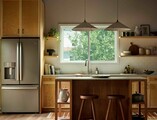 Modern kitchen with warm wood cabinetry and a central island, illuminated by natural light from a large Vanguard Series horizontal slider window above the sink, showing leafy green trees outside.