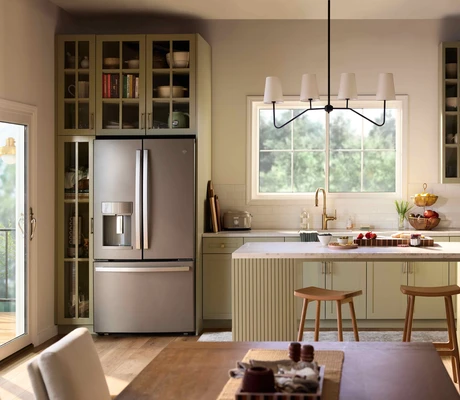 A bright, modern kitchen with sage-green cabinetry, a central island with stools, stainless steel refrigerator, and open shelving, illuminated by natural light from a Restorations Series Horizontal sliding window and a glass door leading to an outdoor deck.