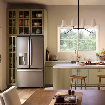 A bright, modern kitchen with sage-green cabinetry, a central island with stools, stainless steel refrigerator, and open shelving, illuminated by natural light from a Restorations Series Horizontal sliding window and a glass door leading to an outdoor deck.